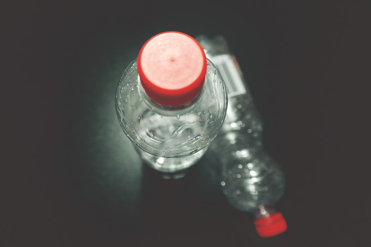 Top view of two clear plastic bottles with red caps on a dark surface, highlighting recycling.